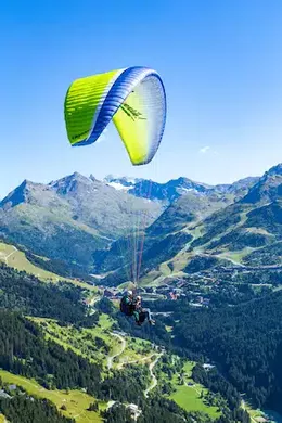 Parapente biplace en vol au-dessus de la vallée de Méribel, sommets et forêts en arrière-plan.